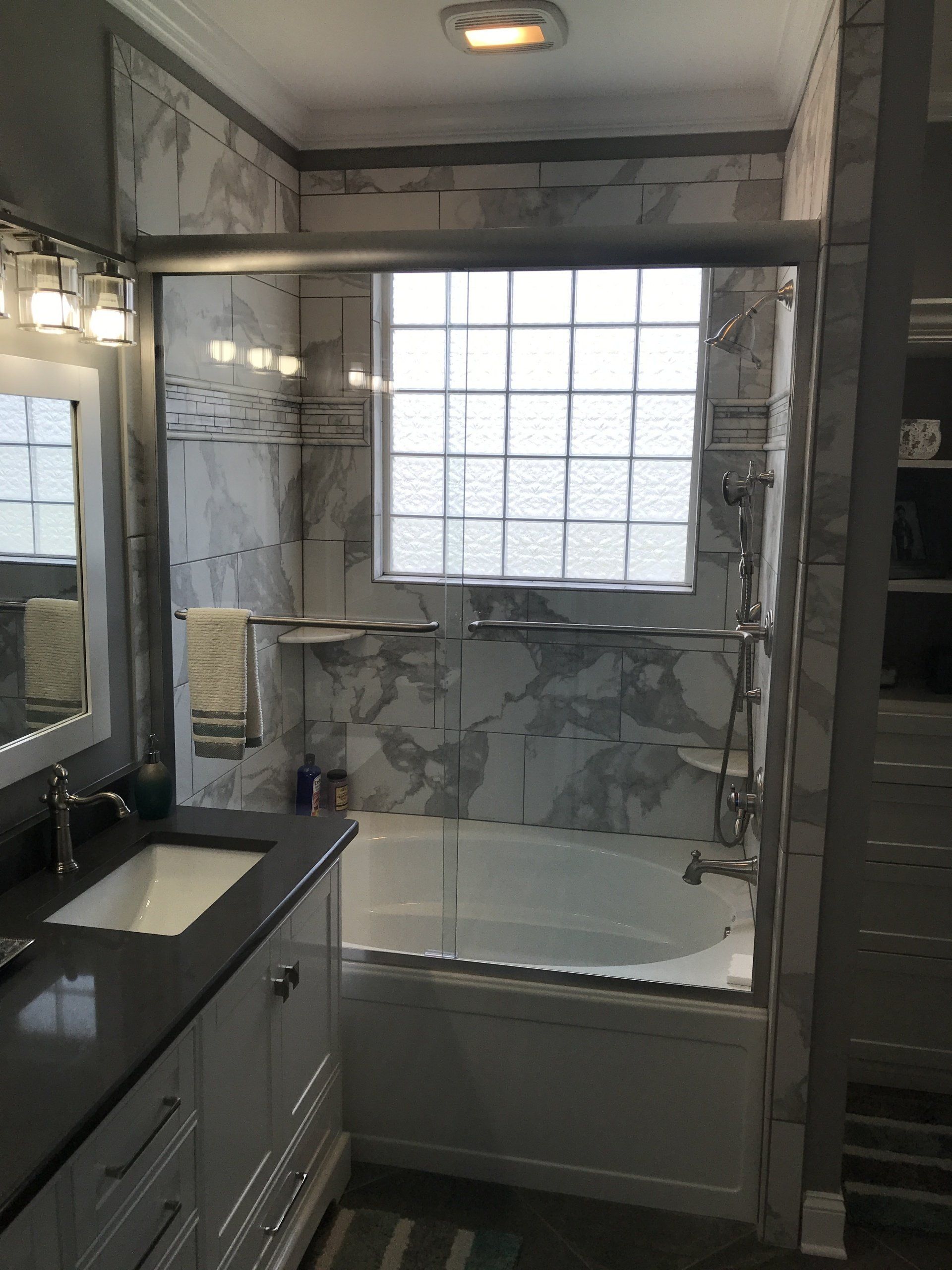 Bathroom with marble-patterned walls, glass shower doors, and a vanity with a dark countertop.