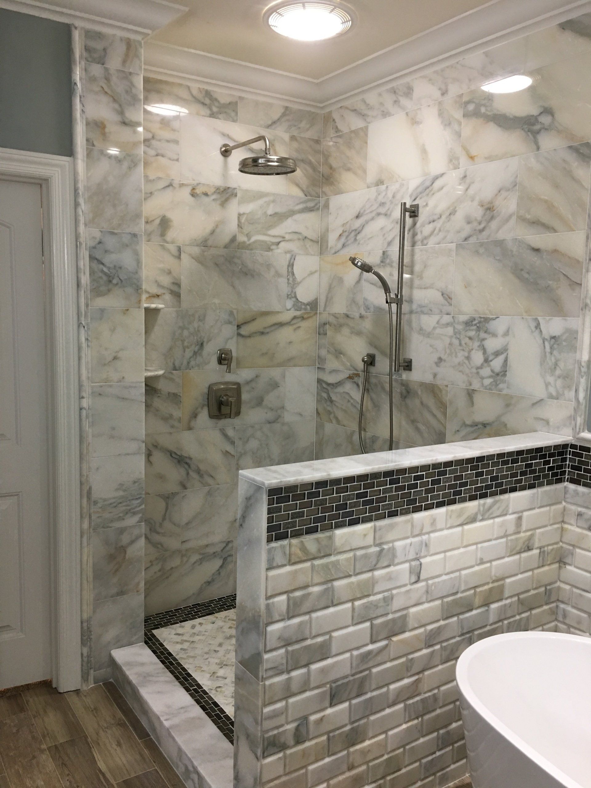 Marble shower with grey, white, and black tile. A shower head and hand shower are mounted.