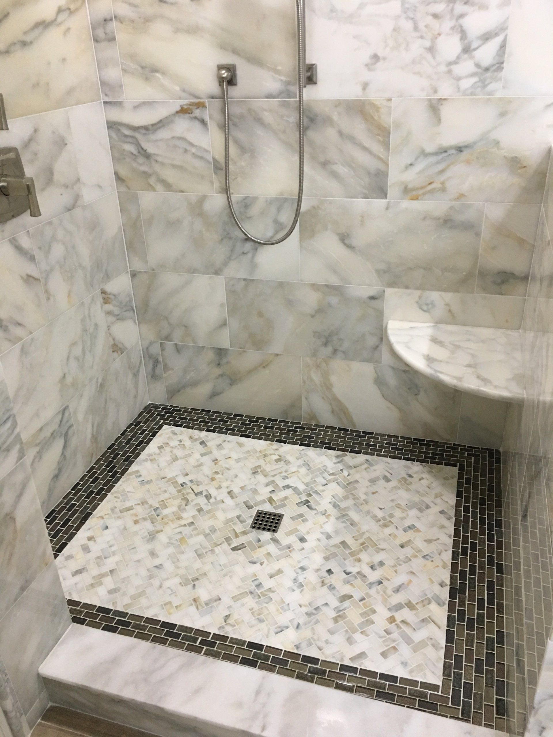 Marble-tiled shower stall with stone mosaic floor, silver fixtures, and built-in shelf.