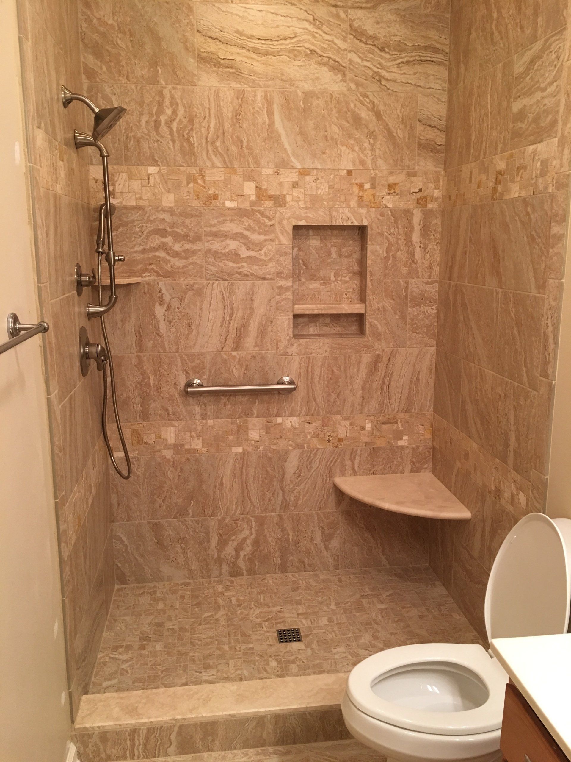 Accessible tiled shower with grab bar, corner seat, and recessed shelf.