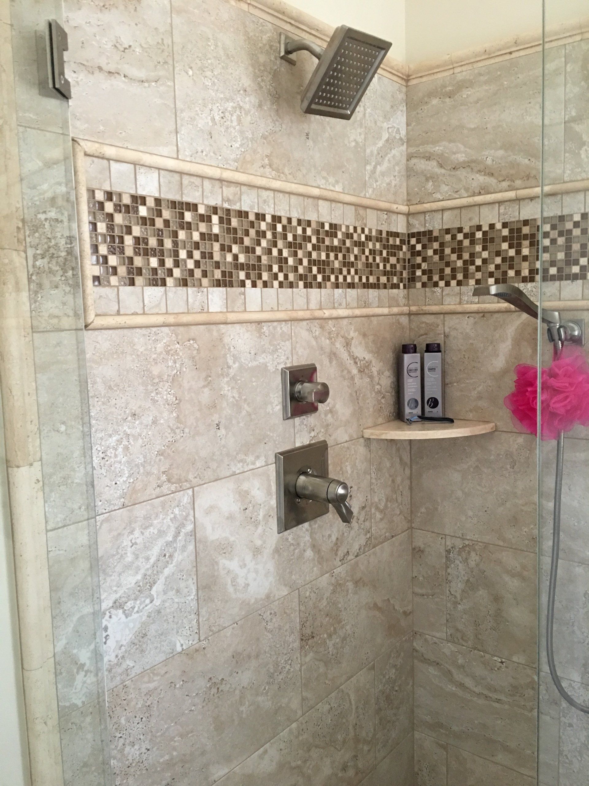 Shower with beige tile, a decorative tile band, and silver fixtures.
