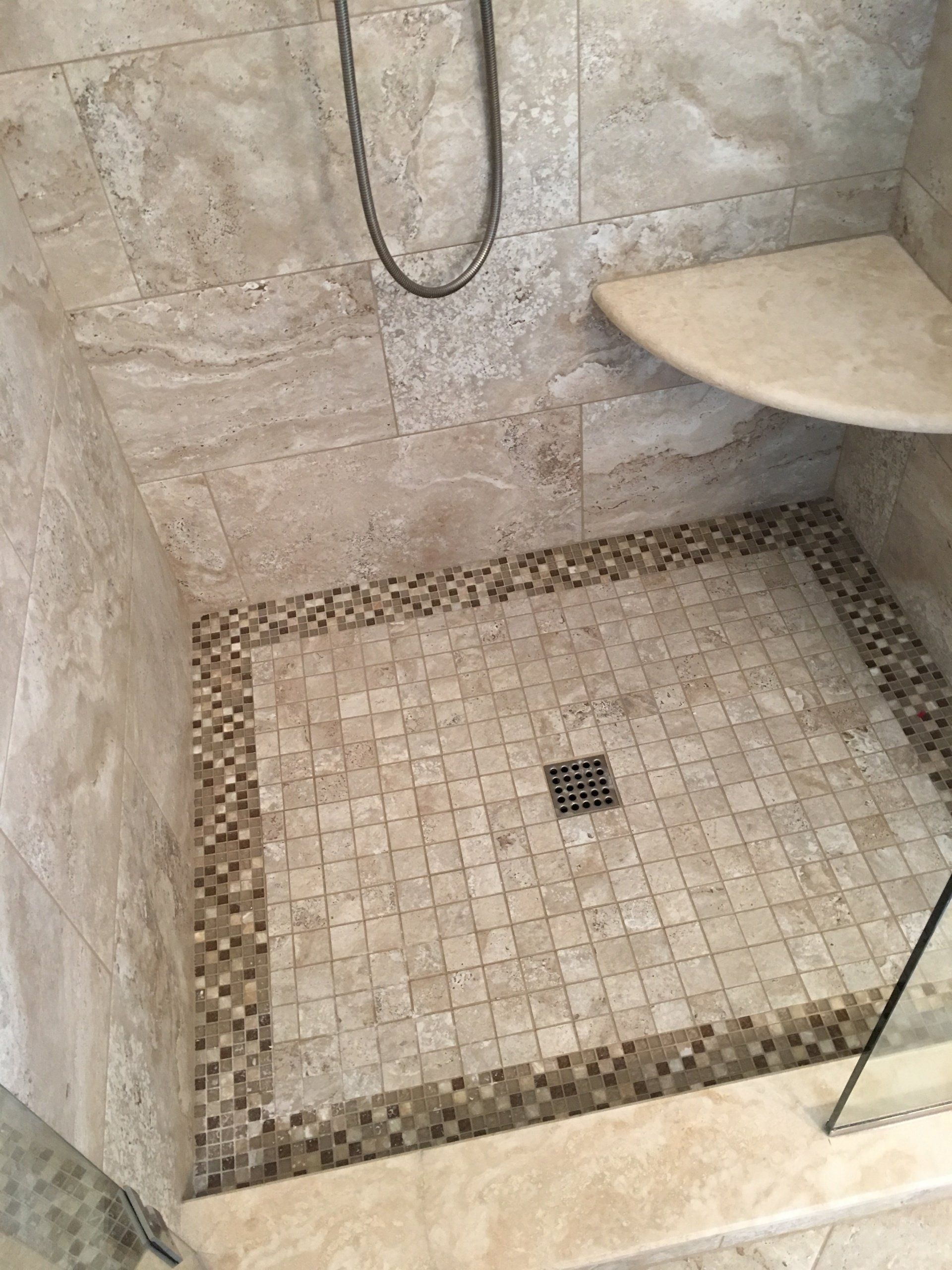 Shower with beige tile, corner seat, and mosaic border. Showerhead visible.