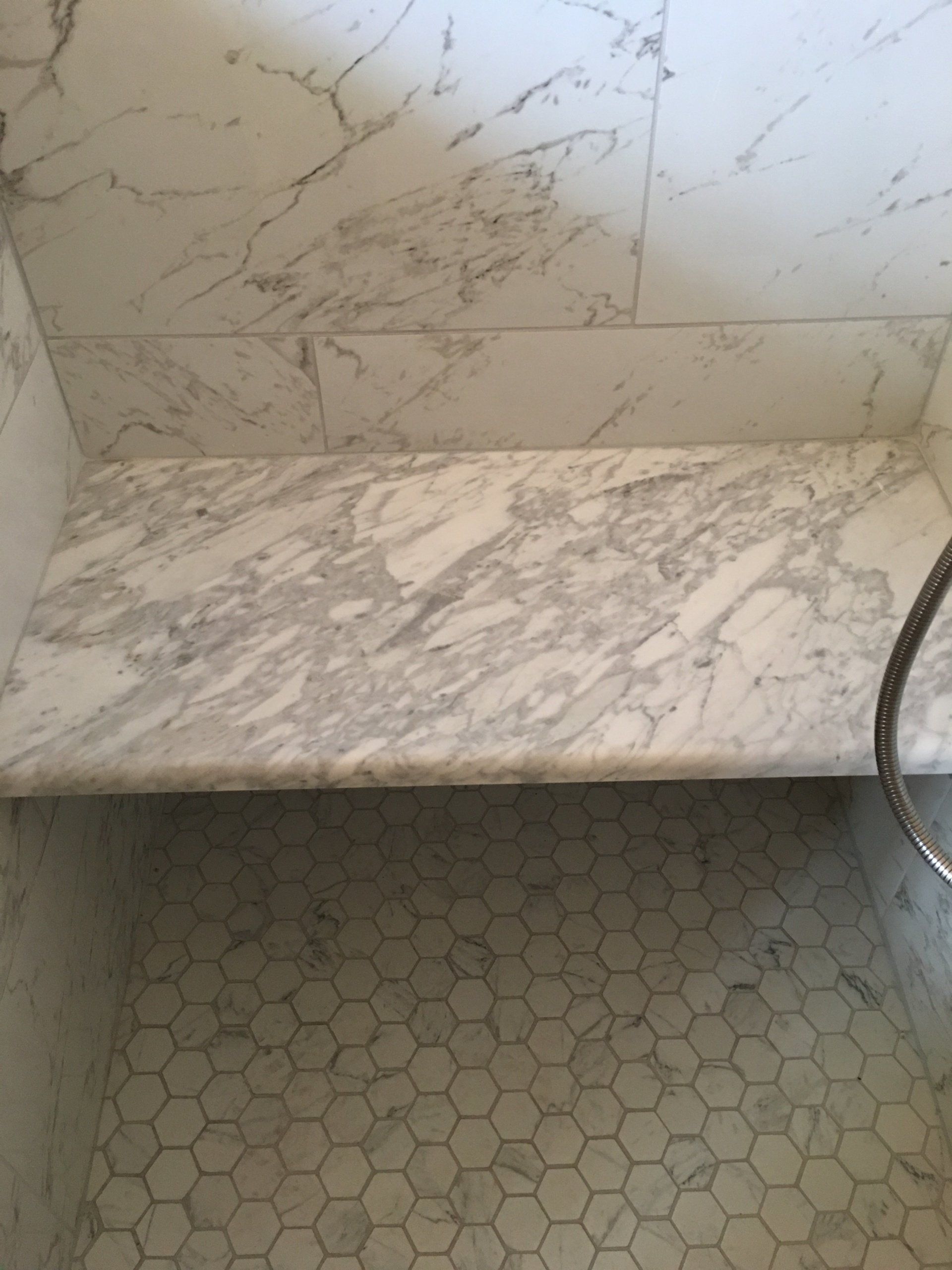 Marble shower with hexagonal floor tiles and a built-in bench.