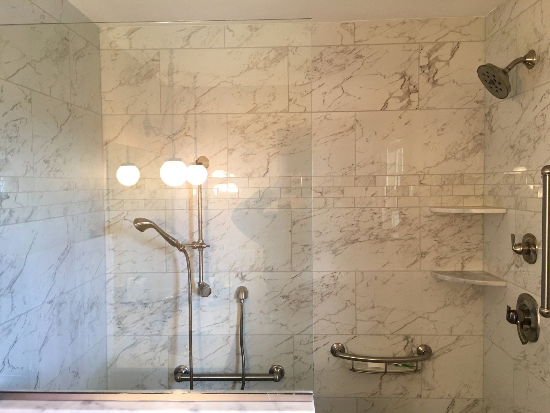 Marble-tiled shower with a hand shower, grab bar, and corner shelves for accessibility.