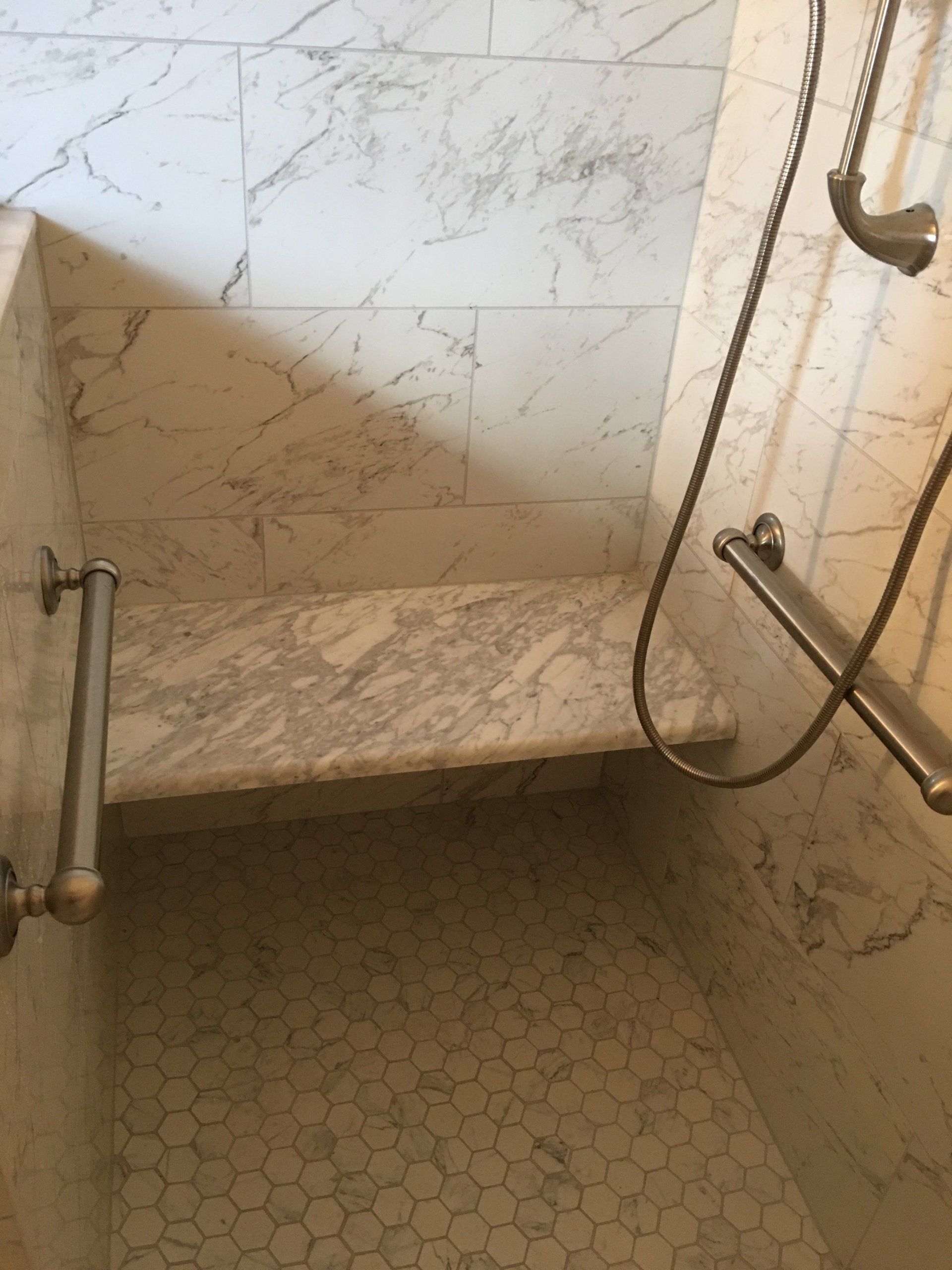 Marble shower with built-in bench, grab bars, and textured floor.