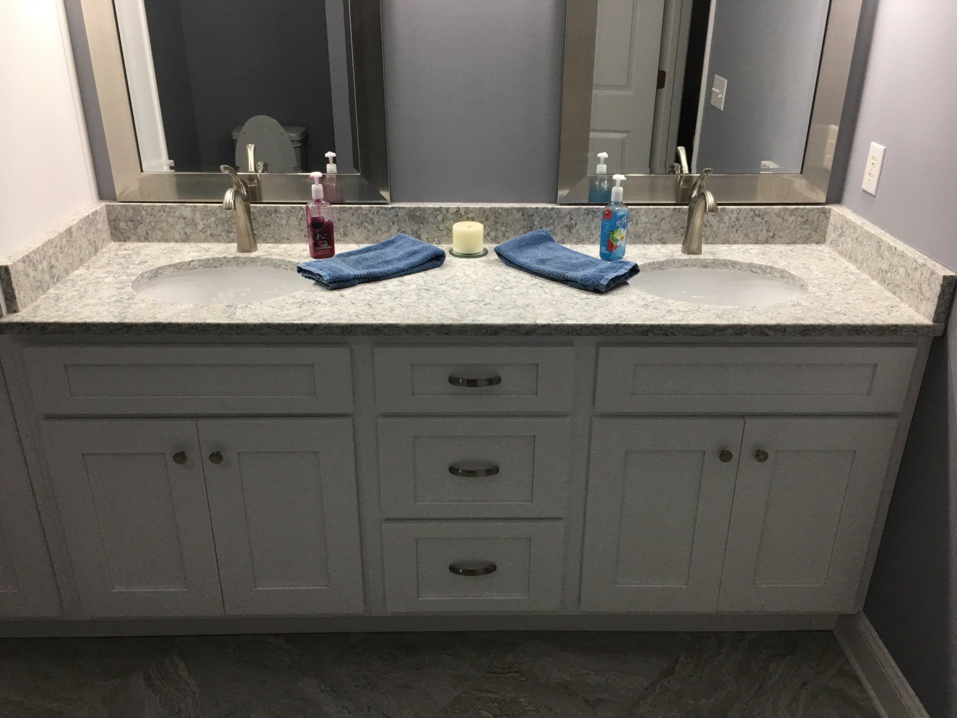 Double vanity with white cabinets, granite countertop, and two sinks. Mirrors, towels, and soap bottles are visible.