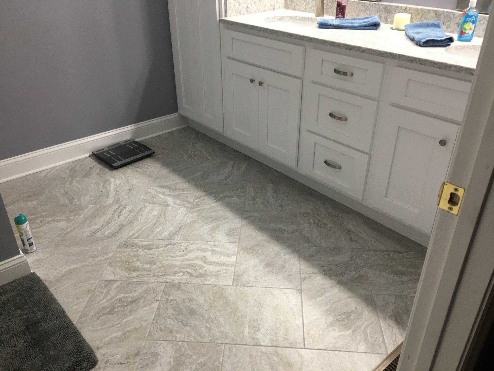 Bathroom with gray walls, white cabinets, and patterned gray tiled floor. A scale and towels are visible.