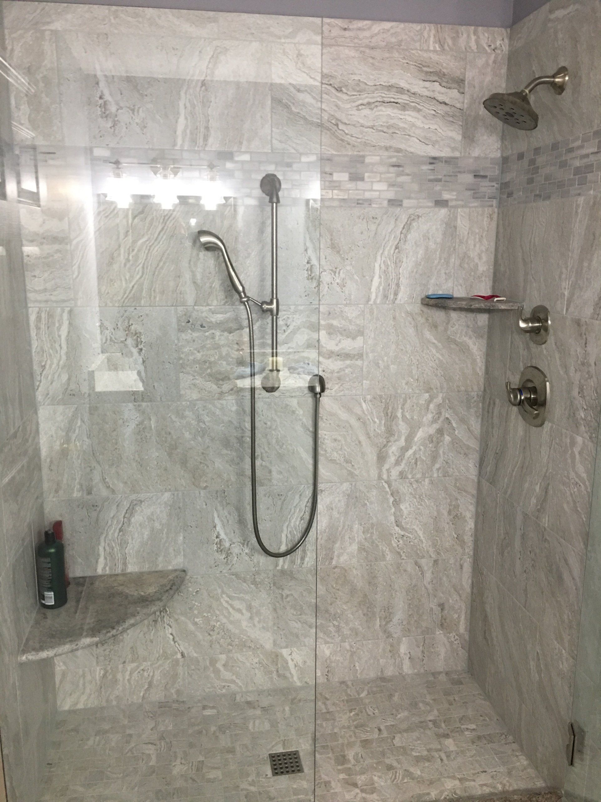 Gray-tiled shower with glass door, handheld showerhead, and built-in soap shelves.