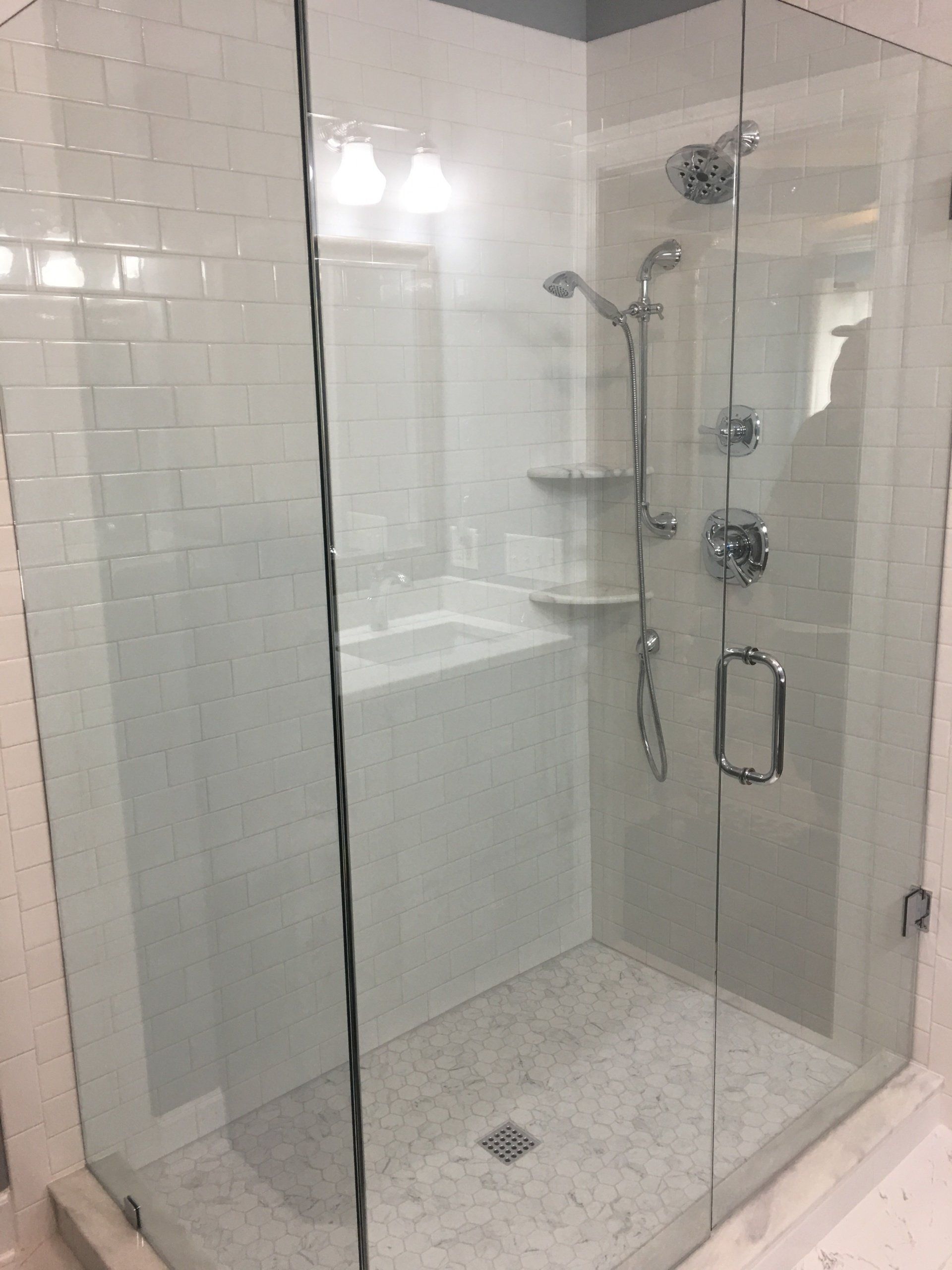 Glass-enclosed shower with white tile walls, stone floor, and chrome fixtures.