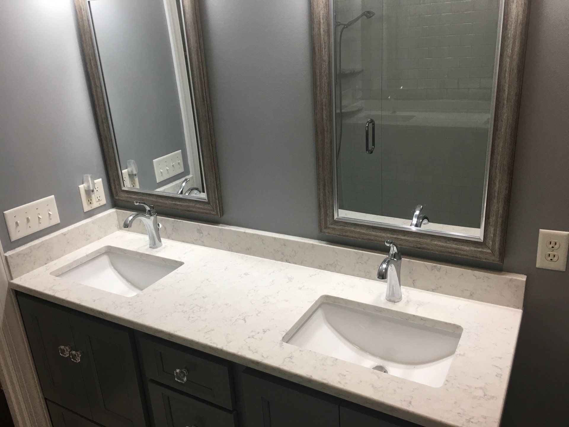 Gray bathroom with double vanity, quartz countertop, and two framed mirrors.