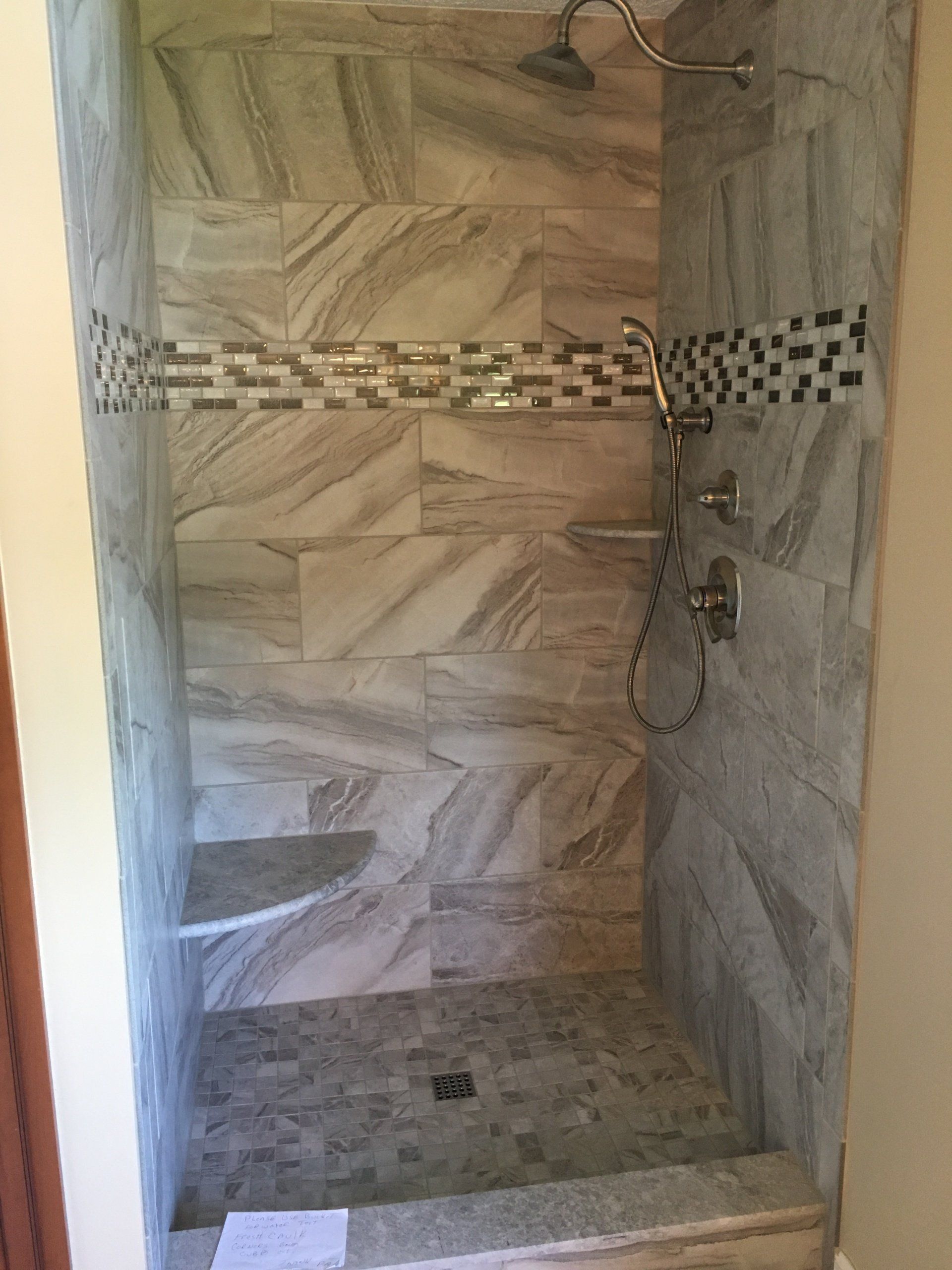 Tiled shower with gray and white marbled walls, a decorative tile band, and two shelves.
