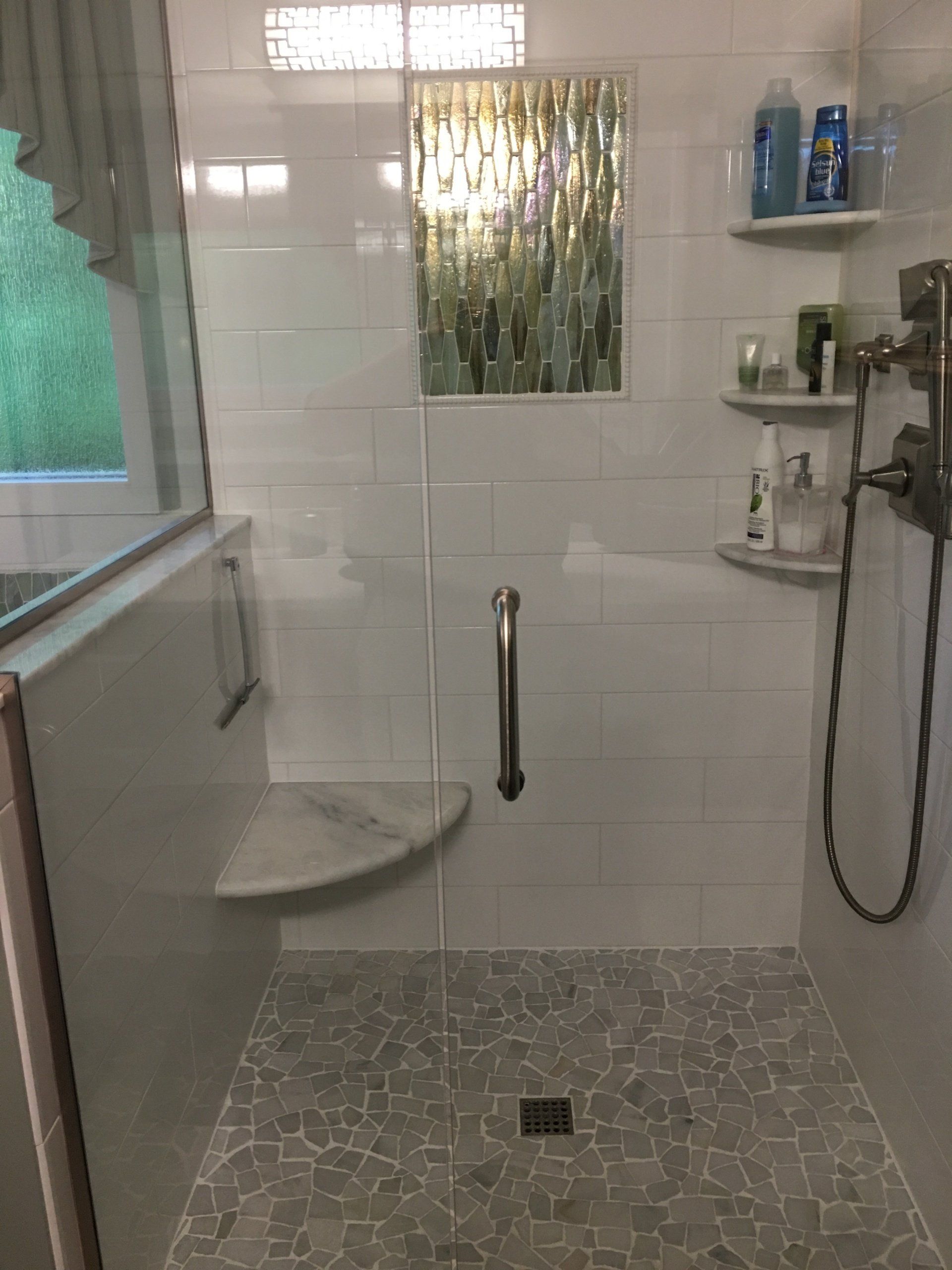 A tiled shower with glass door, built-in bench, and decorative glass window.