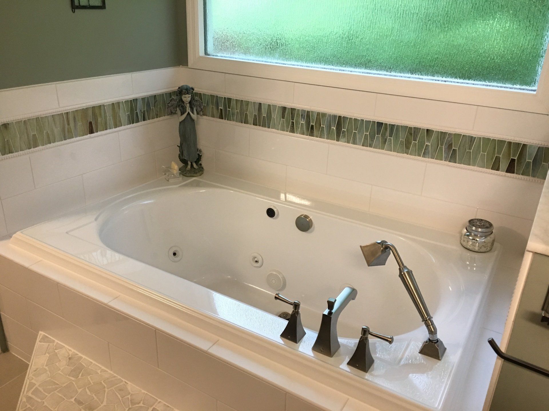 White jacuzzi tub with bronze fixtures and green accent tile under a frosted window.