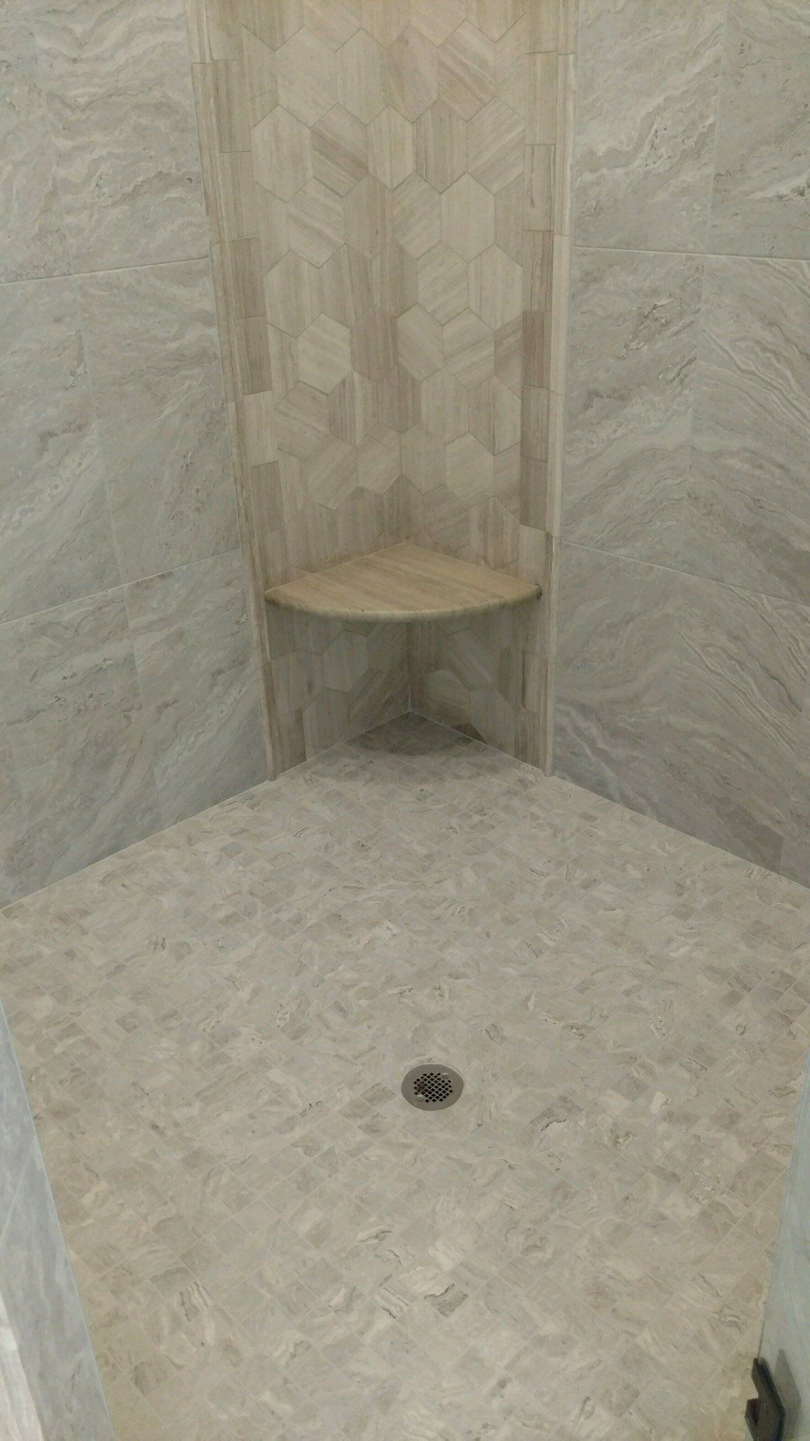 Corner shower with light-colored tile and a built-in shelf; drain visible in the floor.