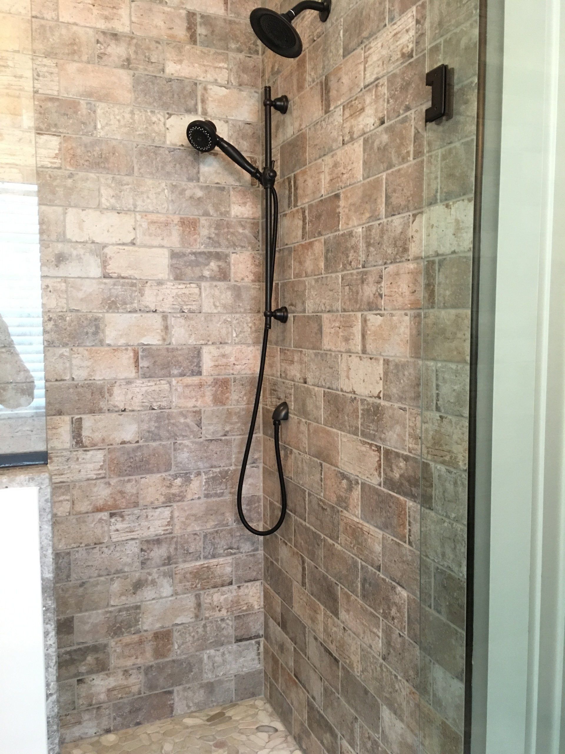 Shower with brown brick-style tile and black shower fixtures.