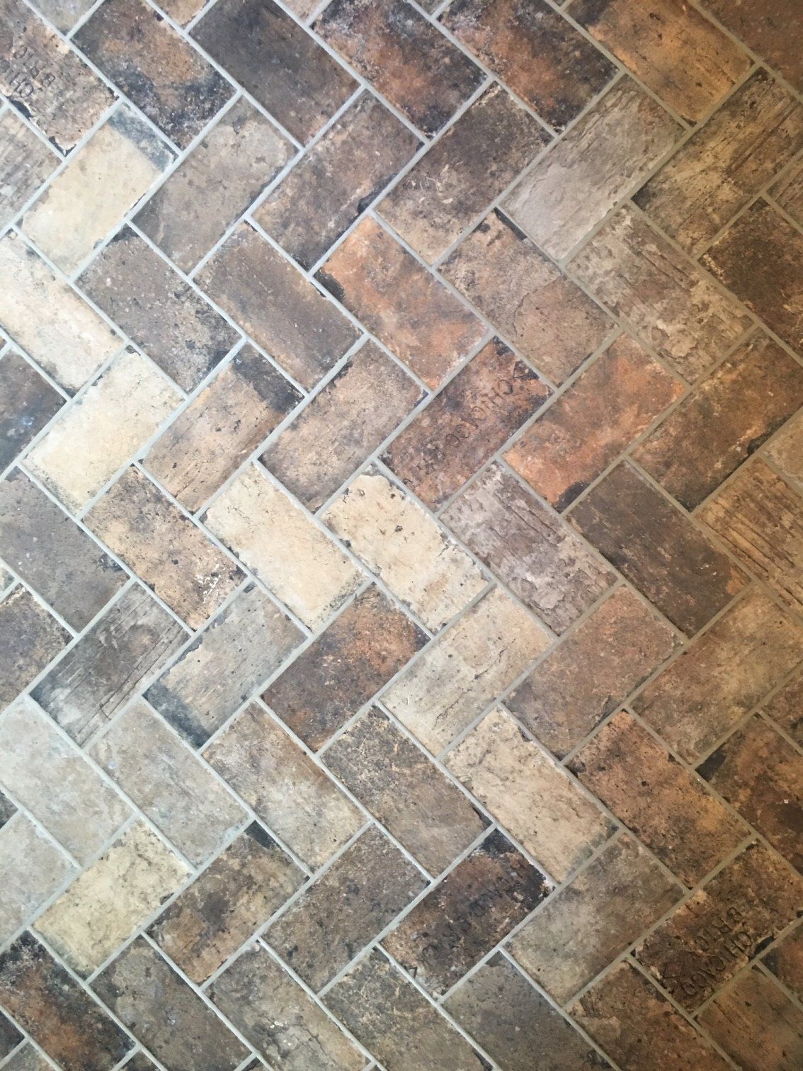 Herringbone pattern brick floor in shades of brown, beige, and black.