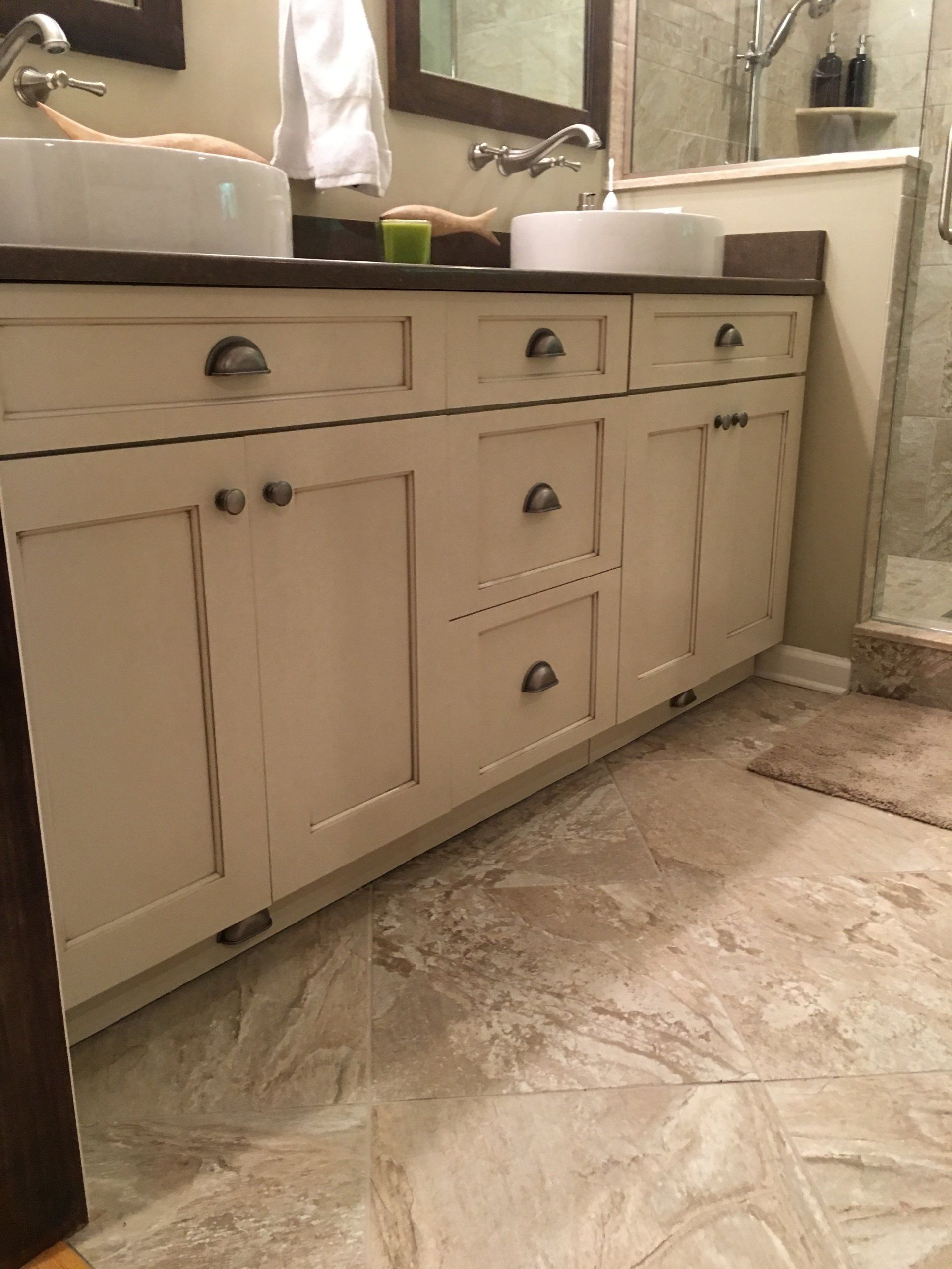 Cream-colored bathroom vanity with two sinks, brown countertop, and stone-like floor.