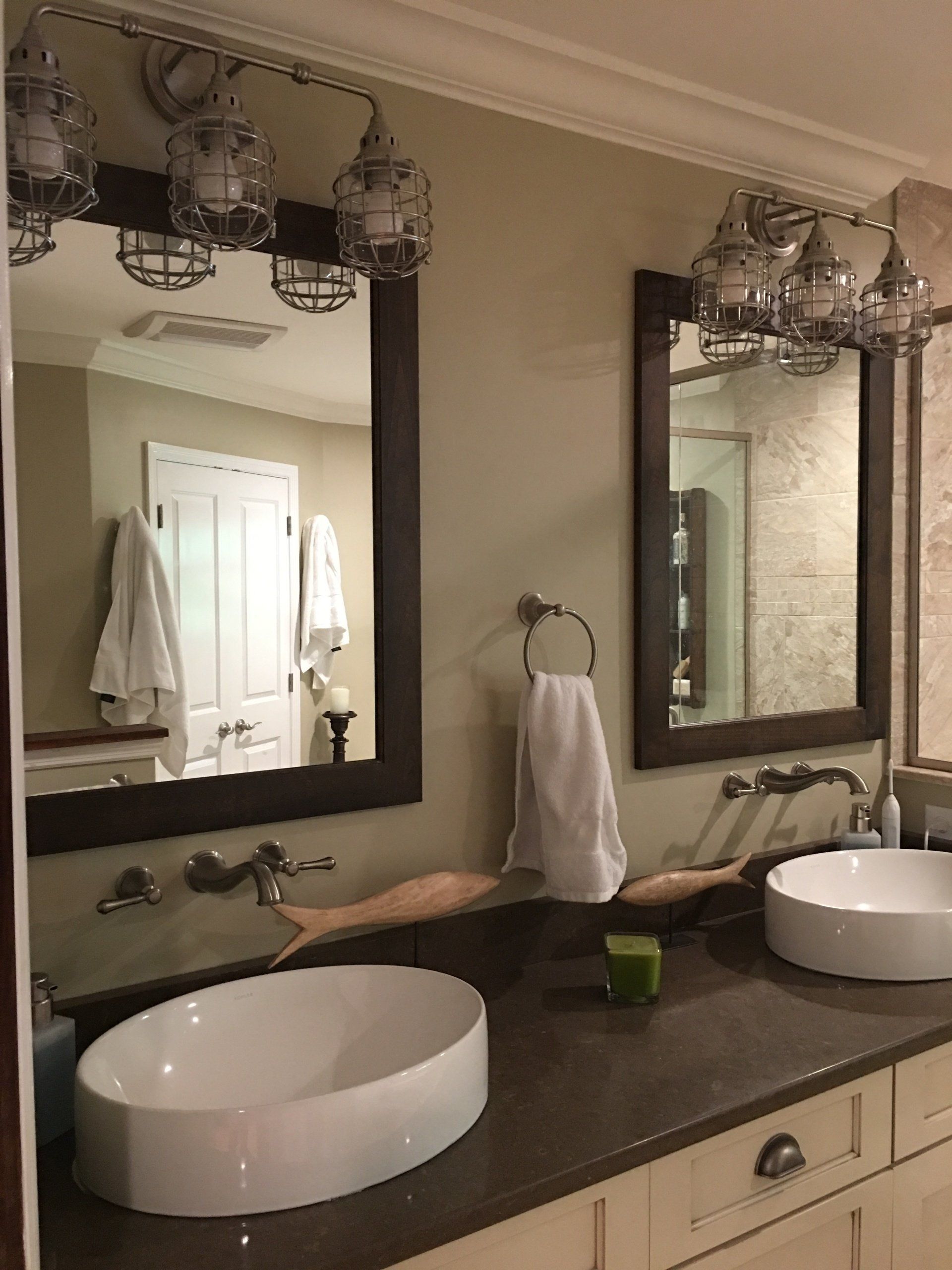 Bathroom with two sinks, mirrors, and industrial-style light fixtures. White sinks, dark countertops, beige walls.
