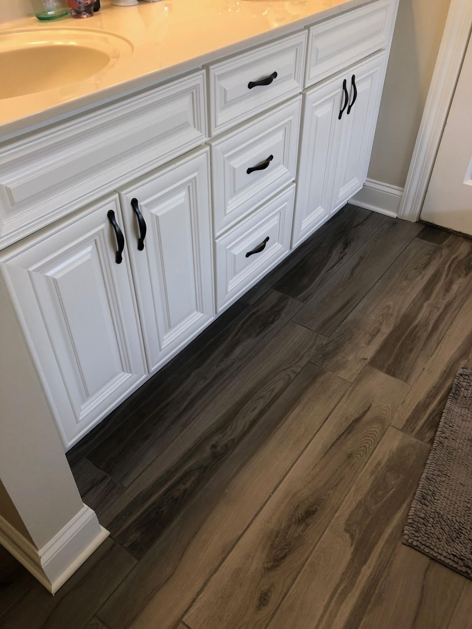 White bathroom vanity with black hardware, dark wood-look floor.