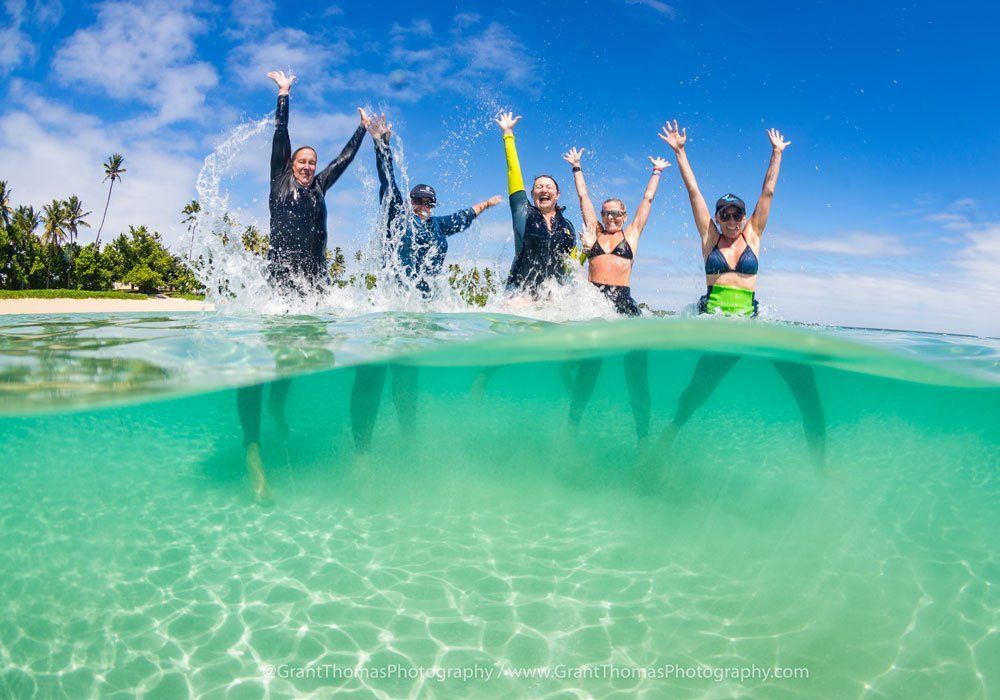 People jumping into clear turquoise ocean near a tropical beach under a blue sky