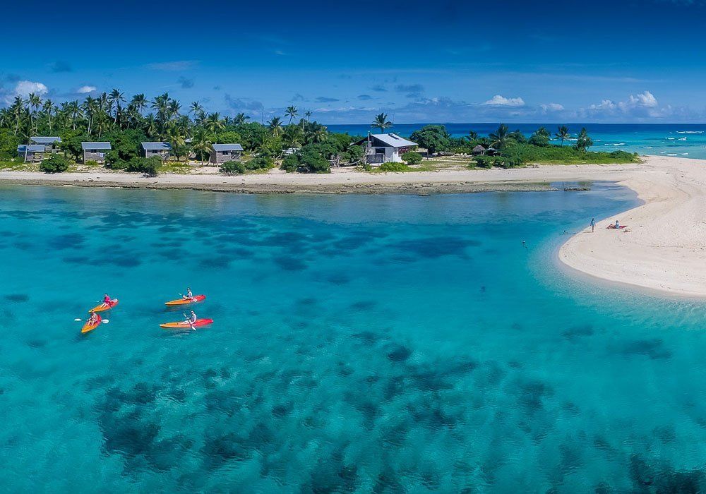 Tropical island lagoon with turquoise water, sandy shore, and two people kayaking near the beach.