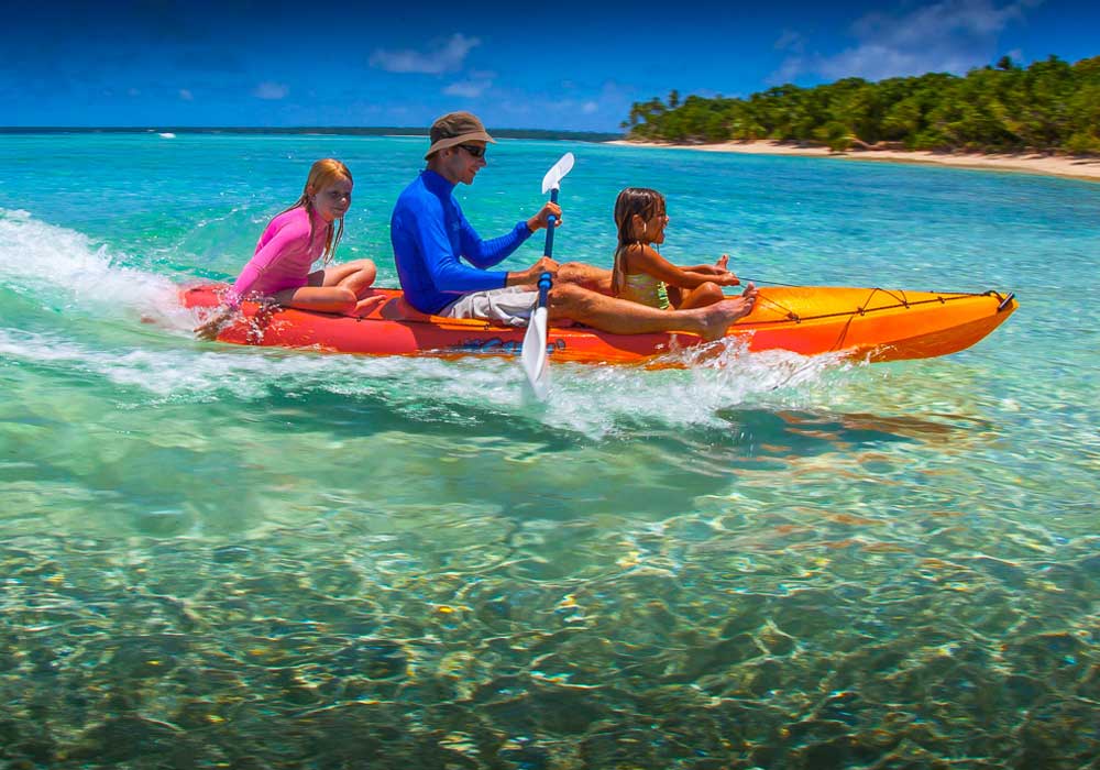 Three people kayaking in clear turquoise water near a tropical beach