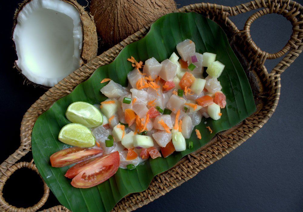 Assorted seafood salad on a banana leaf tray with lime wedges and tomato slices, served on a woven mat