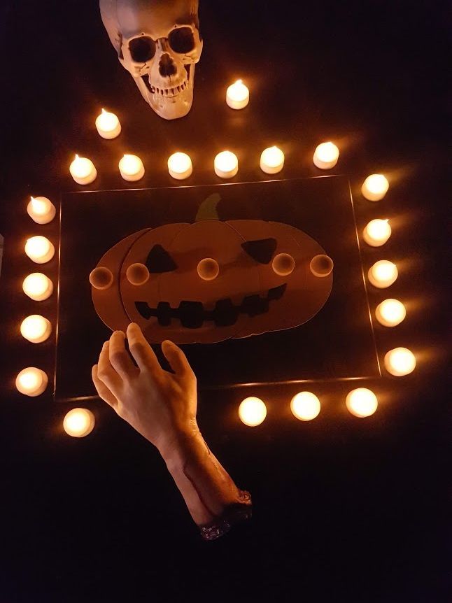 Halloweentafereel: pompoen en skelet in kaarsen, met een afgehakte arm.