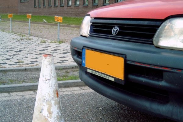 Rode autobumper met een oranje kentekenplaat en een verkeerskegel.