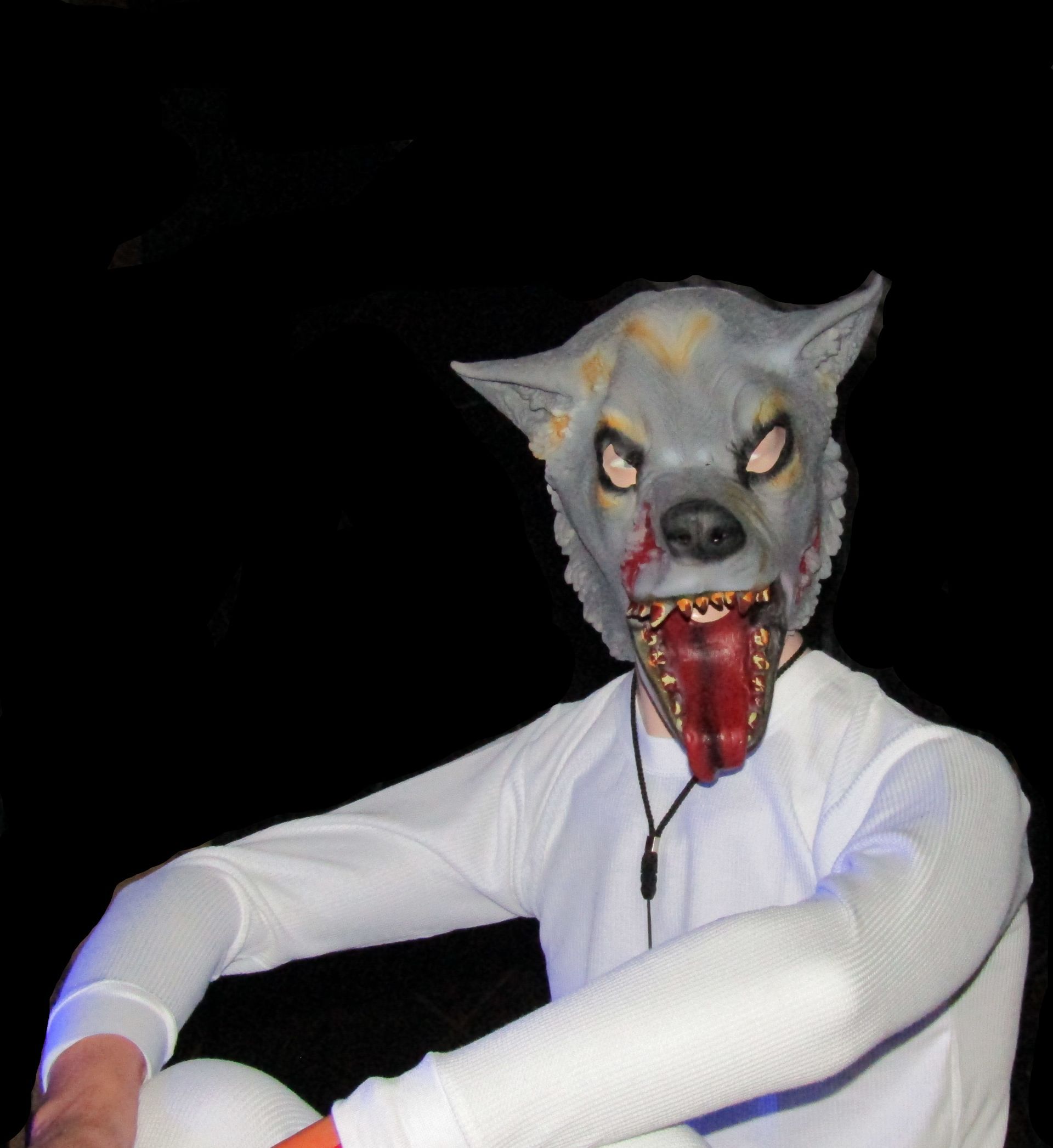 Persoon met een grijs wolvenmasker, bloederige open mond, wit shirt met lange mouwen, donkere achtergrond.