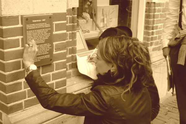 Vrouw leest plaquette op bakstenen gebouw.