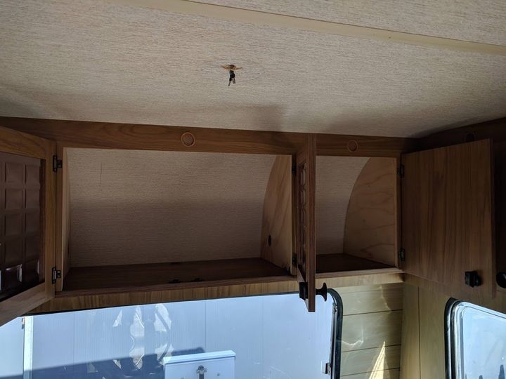 Kastjes in een camper, met openslaande deuren, langs de wand boven een raam. Houten afwerking en een lichtgekleurd interieur.