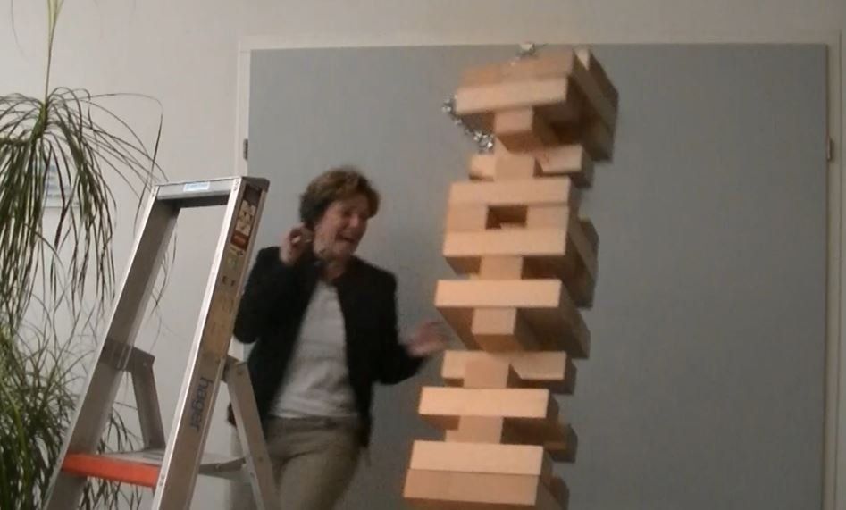 Vrouw reageert op een grote Jenga-toren die op het punt staat om te vallen, naast een ladder.