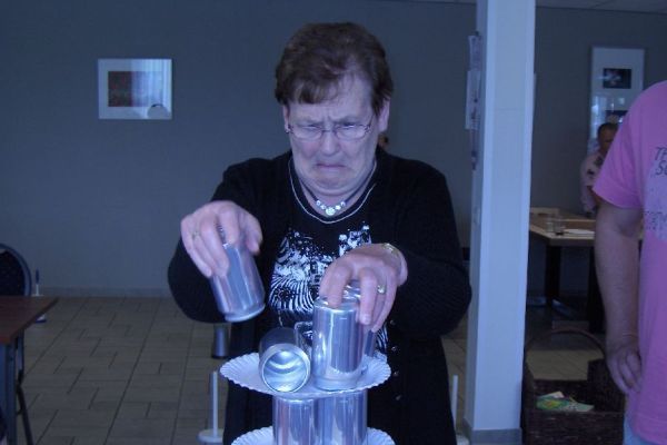 Een vrouw stapelt zorgvuldig blikken op een verhoogd platform en concentreert zich intensief. Binnen, neutrale achtergrond.
