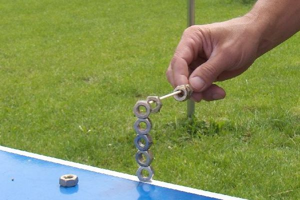 Een hand die een bout vasthoudt, balanceert een stapel moeren op een tafel tegen een groen gazon.