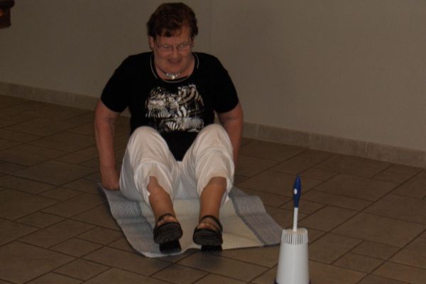 Een persoon zit op een mat op een tegelvloer, vlakbij een toiletborstel.