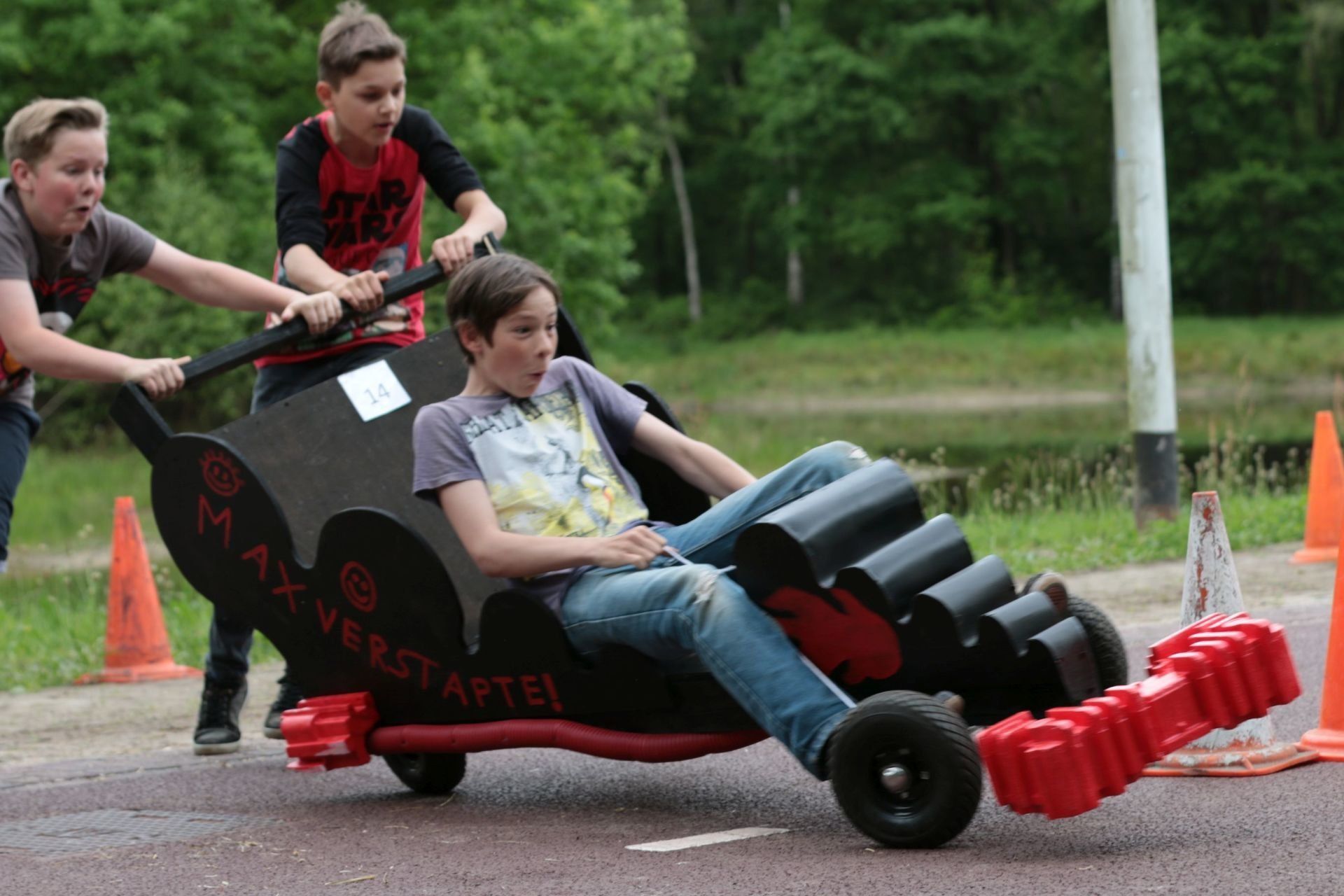 Jongens duwen een zelfgemaakte auto met een persoon erin voort tijdens een buitenwedstrijd.