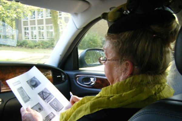 Een persoon in een auto bestudeert een schema van de bedieningselementen, mogelijk ter voorbereiding op een rijexamen.