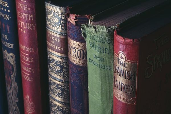 Close-up van een rij oude boeken. Rode, blauwe en groene ruggen zijn zichtbaar, met verschillende gradaties van slijtage.