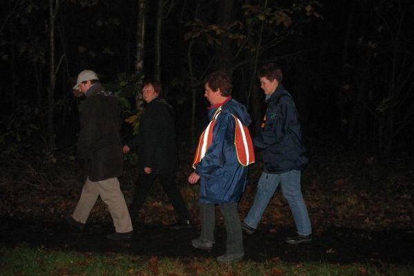 Vier mensen lopen over een donker pad in een bos. Eén van hen draagt ​​een reflecterend vest.