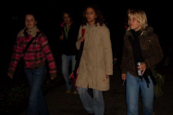 Vier mensen lopen 's nachts, ogenschijnlijk op een pad; het is er zwak verlicht.