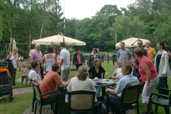 Mensen verzamelen zich rond tafels onder parasols in een buitenomgeving, waar ze gezellig met elkaar praten en van de dag genieten.