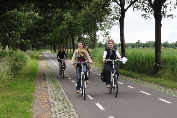 Vier mensen fietsen over een geplaveid pad dat omzoomd is met bomen en gras.