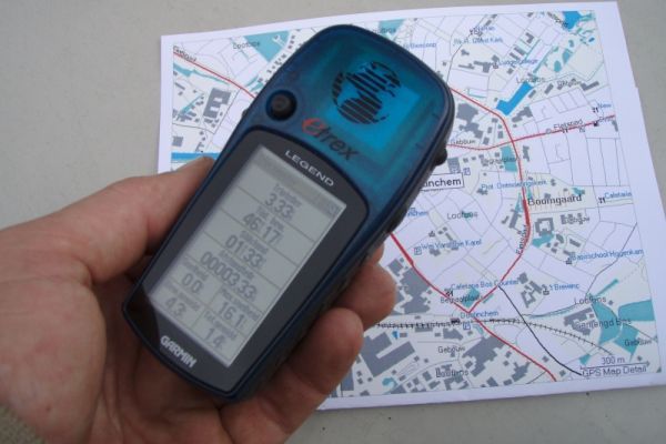 Hand die een blauw GPS-apparaat boven een afgedrukte kaart houdt, waarschijnlijk voor navigatie.
