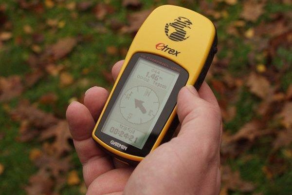 Hand die buiten een geel Garmin eTrex GPS-apparaat vasthoudt, waarop kompas en gegevens worden weergegeven.