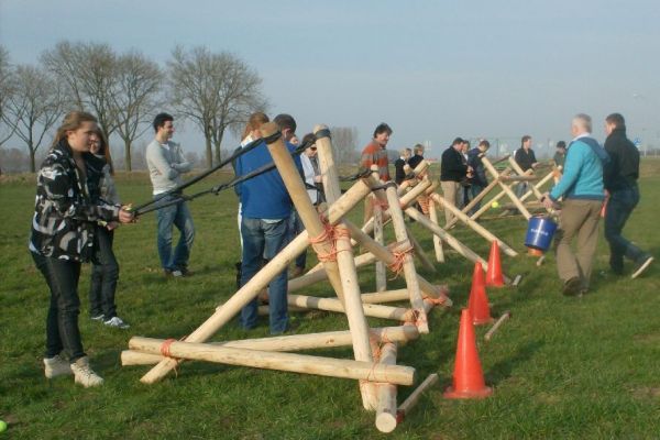 Mensen bedienen houten katapulten op een grasveld en richten op oranje kegels.