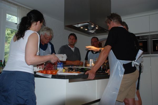 Mensen koken samen in een keuken. Een vrouw snijdt voedsel. Mannen kijken toe.