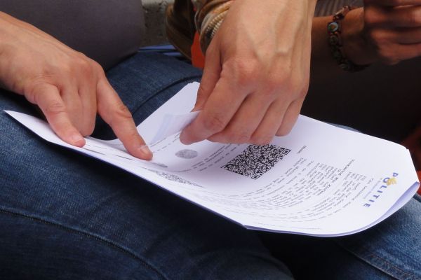 Handen wijzen naar een papier met een QR-code erop, dat op iemands schoot ligt.