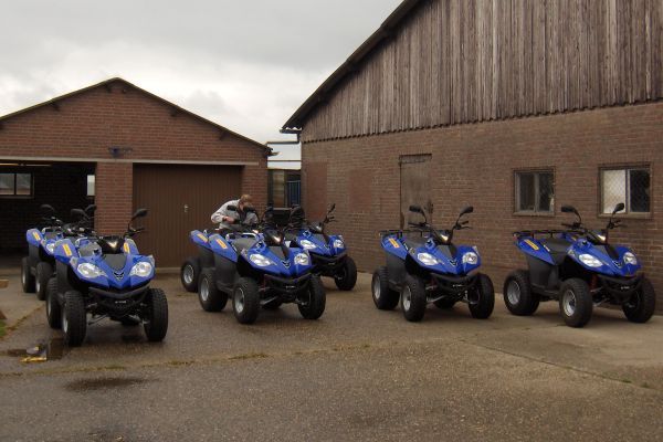 Blauwe quads staan ​​geparkeerd voor een bakstenen gebouw. ​​Eén persoon zit op een van de voertuigen.