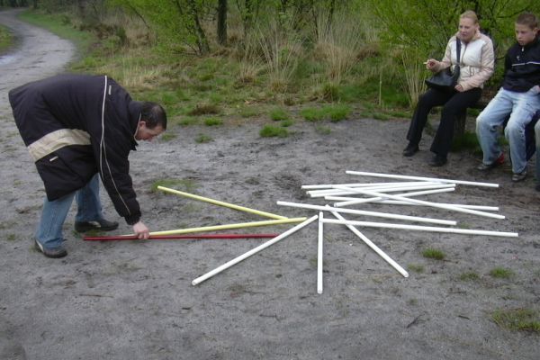 Iemand die takken op de grond schikt, twee mensen die in de buurt op een bankje zitten, buitenomgeving.